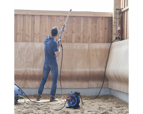 Un homme utilise un nettoyeur haute pression dans une pièce avec des murs en bois et un enrouleur de câble électrique
