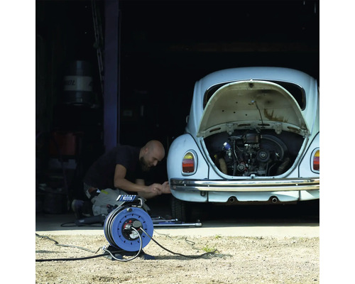 Mann repariert ein Auto mit geöffneter Motorhaube und benutzt eine Kabeltrommel