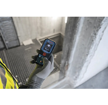 Main gantée tenant un télémètre Bosch dans un bâtiment en construction.