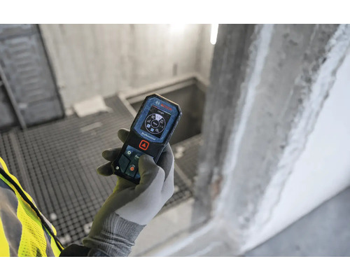 Main gantée tenant un télémètre Bosch dans un bâtiment en construction.