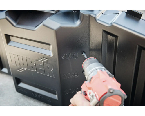 Un homme perce un trou dans une cuve de récupération d''eau de pluie Huber noire.