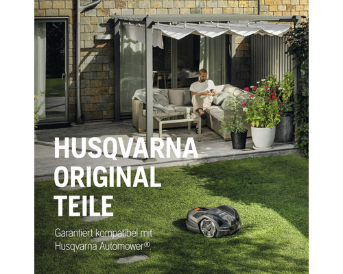 Husqvarna Automower auf Rasen vor einem Haus mit Terrasse und Person.