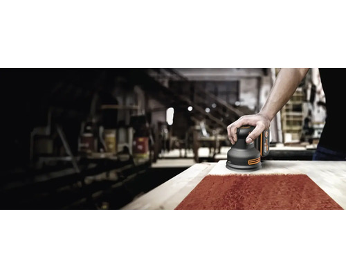 Un homme ponce du bois avec une ponceuse excentrique dans un atelier.