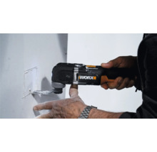 Ein Mann benutzt einen Multifunktionsschneider von Worx, um einen rechteckigen Ausschnitt in eine weiße Wand zu schneiden.