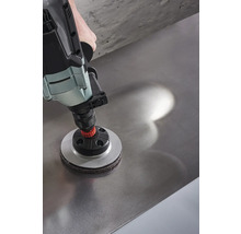 Une perceuse avec un accessoire de ponçage est utilisée sur une surface métallique.