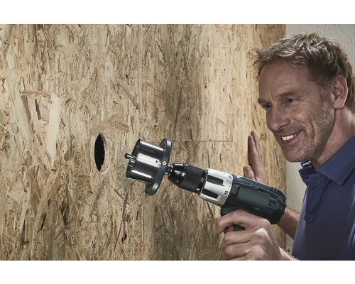 Un homme perce un trou dans une plaque de bois avec une scie cloche.
