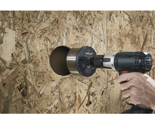 Une personne perce un trou dans une plaque de bois avec une scie cloche