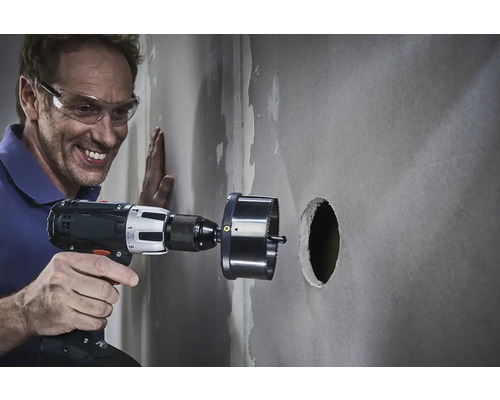 Un homme perce un trou dans un mur avec une scie cloche