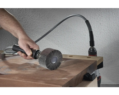 Person verwendet eine Schleifmopbürste auf einem Holzbrett, angetrieben von einer Bohrmaschine.