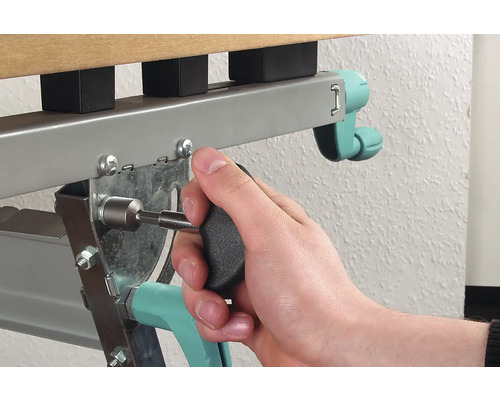 Une personne fixe une vis avec un tournevis sur un cadre de lit en métal.