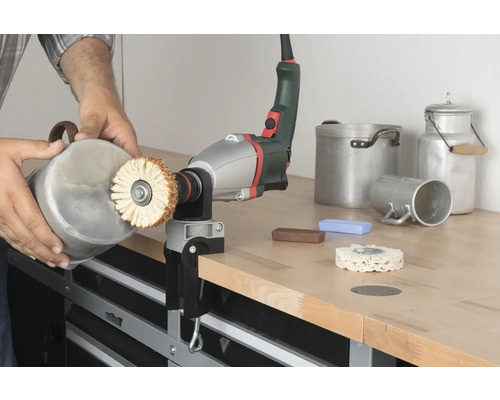 Eine Person poliert einen Behälter mit einer Poliermaschine auf einer Werkbank.