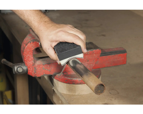 Eine Person schleift ein Rohr mit einem Schleifschwamm, das in einem Schraubstock befestigt ist.
