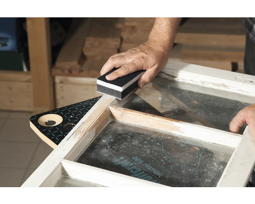 Eine Person schleift einen Fensterrahmen mit einem Schleifklotz.