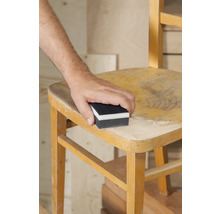 Une personne ponce une chaise en bois avec un bloc de ponçage
