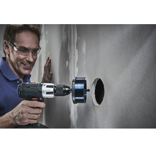 Handwerker bohrt mit einer Lochsäge ein Loch in eine Wand