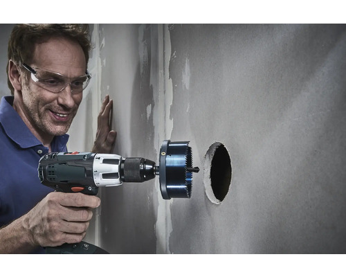 Un artisan perce un trou dans un mur avec une scie cloche