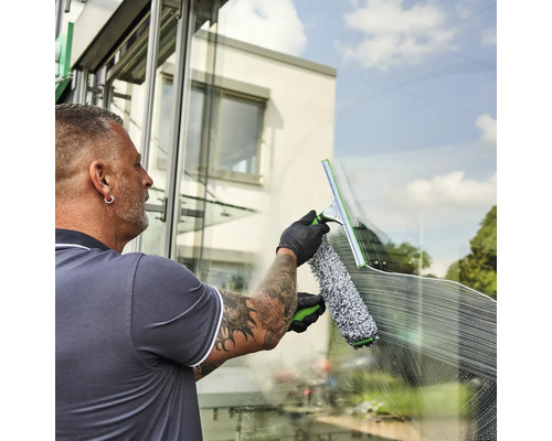 Mann reinigt Fenster mit Fensterwischer und Einwascher.