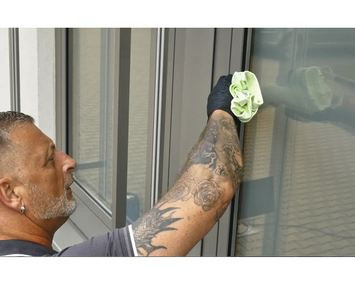 Mann mit Tattoos reinigt Fenster mit einem Tuch