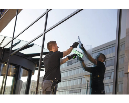 Un homme nettoie une grande façade vitrée avec un lave-vitre et une éponge.