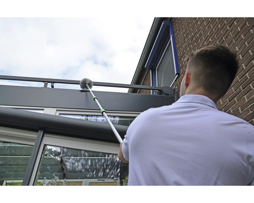 Mann reinigt ein Terrassendach mit einem Teleskopstiel und einer Bürste