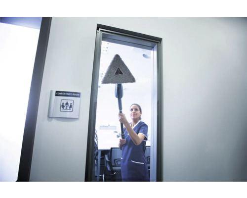 Eine Frau reinigt ein Fenster mit einem dreieckigen Mopp in einem Konferenzraum.