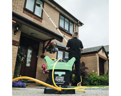 Außenaufnahme eines Fensterputzers, der mit einem Fensterreinigungsgerät Fenster putzt