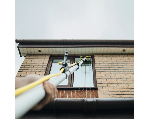 Fensterreinigung mit Teleskopstielbürste an einem Haus