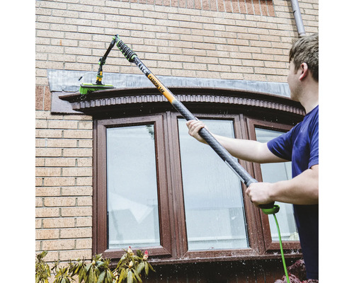 Fensterreinigung mit Teleskopstielbürste an einem Haus.