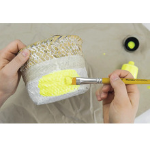 Une personne peint un panier à plantes avec un pinceau et de la peinture jaune.