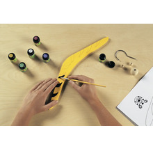 Un boomerang jaune est peint avec de la peinture et un pinceau, le matériel de bricolage est prêt.