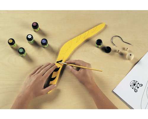 Un boomerang jaune est peint avec de la peinture et un pinceau, le matériel de bricolage est prêt.