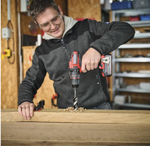 Ein Mann bohrt mit einem Akku-Bohrschrauber ein Loch in ein Holzbrett.