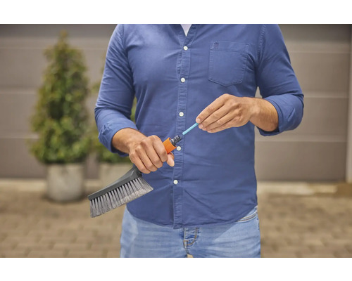 Eine Person schliesst eine Bürste an einen Gartenschlauch an