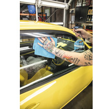 Eine Person reinigt eine gelbe Autoscheibe mit Glasreiniger und einem Tuch.