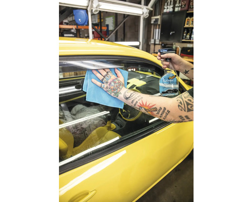 Eine Person reinigt eine gelbe Autoscheibe mit Glasreiniger und einem Tuch.