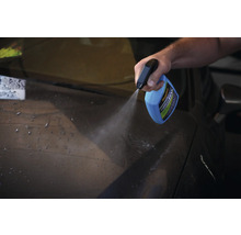 Eine Person sprüht Autowachs aus einer Sprühflasche auf ein Auto.