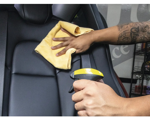 Reinigung eines Autositzes mit Reinigungsmittel und Tuch.