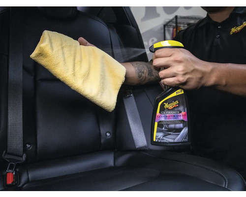 Person reinigt Autositz mit Lederreiniger und Tuch