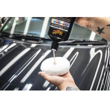 Eine Person trägt Polierpaste von Meguiars auf ein Polierpad auf, um ein Auto zu polieren.