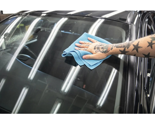 Ein Mann wischt die Windschutzscheibe eines Autos mit einem Mikrofasertuch ab.