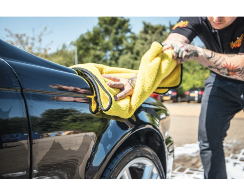 Person trocknet ein Auto mit einem Mikrofasertuch