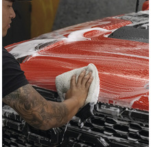 Eine Person reinigt ein rotes Auto mit einem Tuch und Schaum.