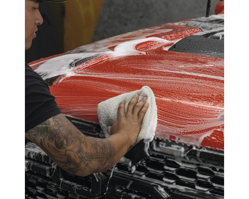 Eine Person reinigt ein rotes Auto mit einem Tuch und Schaum.