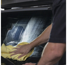 Eine Person reinigt eine Autoscheibe mit einem Tuch.