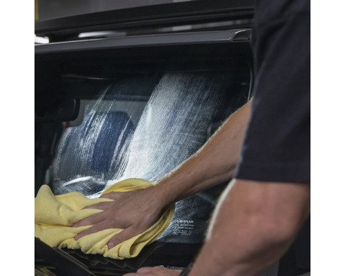 Eine Person reinigt eine Autoscheibe mit einem Tuch.