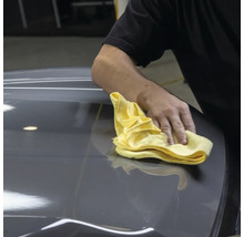 Person reinigt Fahrzeug mit einem Tuch