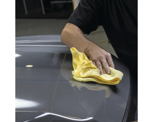 Person reinigt Fahrzeug mit einem Tuch