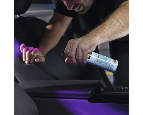 Person sprüht Geruchsneutralisierer in ein Auto.