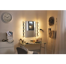 Helles Zimmer mit beleuchtetem Spiegel, Schreibtisch, Dekoration und Uhr an der Wand.