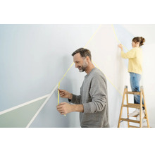Zwei Personen gestalten eine Wand mit Malerkrepp für geometrische Formen.